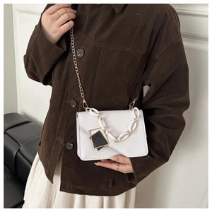 Detail of cream white crossbody bag with gold chain and black geometric charm on model