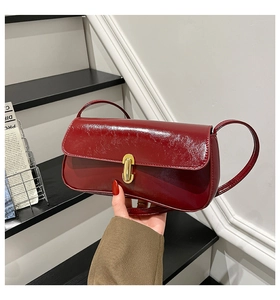 Detail of burgundy patent leather baguette bag with a gold twist lock and a smooth glossy finish