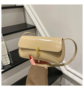 Close-up of beige patent leather shoulder bag with gold cylindrical lock and glossy finish
