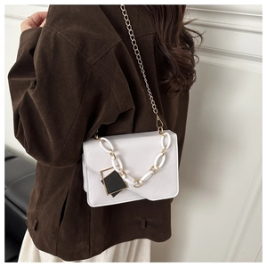 Detail view of a cream chain shoulder bag with double straps on a brown coat