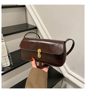 Close-up of vintage dark brown baguette bag with gold lock and oil-wax leather texture