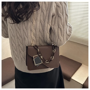 Detail of a brown shoulder bag with gold chain strap and chunky decorative link accessory