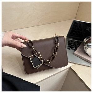 Detail of a dark brown crossbody bag with metal buckle and chain strap on a desk