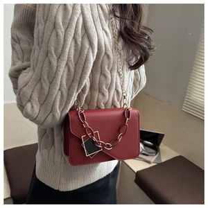 Detailed view of dark red crossbody bag with gold metal and acrylic chain straps