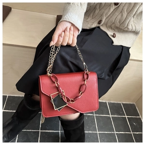 Detail of red PU leather bag featuring a bold chain link and black geometric charm