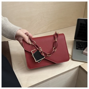 Detail of red crossbody bag with geometric buckle and resin chain strap on desk