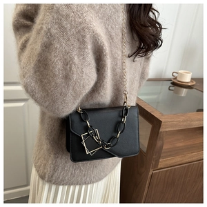 Detail of elegant black crossbody bag with gold chain strap and decorative buckle