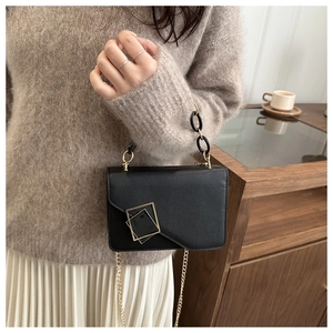 Detail of black leather square bag featuring golden interlocking buckles and chain handle