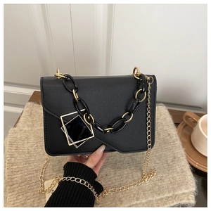 Detail of elegant black crossbody bag with gold chain strap and square buckle on soft rug