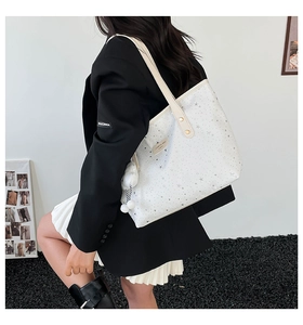 Chic beige tote bag with star patterns and a fluffy pompom detail shown on a shoulder