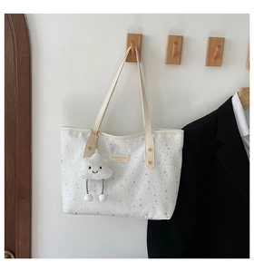 Detail of white star print tote bag featuring a cute cloud plush charm on a wooden hook