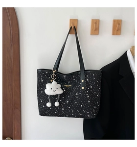 Detail of black star-patterned tote bag with gold logo plaque and fluffy cloud charm