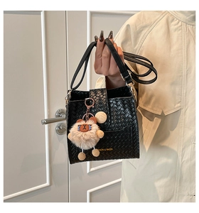 Detail of black woven leather bucket bag with a cute teddy bear charm and gold logo