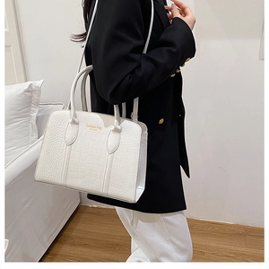 Detail of white crocodile pattern tote bag with gold lettering shown in a city style
