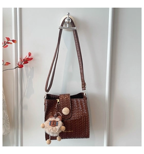 Detail of dark brown woven texture handbag with wooden buckle and bear charm on white wall