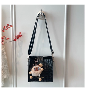Detail of black woven crossbody bag with golden logo and cute bear plush charm hanging