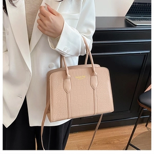 Detail of beige faux crocodile tote bag with gold lettering shown on white suit jacket
