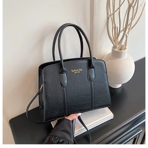 Detail of black crocodile embossed faux leather handbag with golden logo and straps