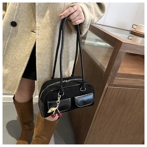 Detail of black suede shoulder bag featuring dual front pockets and cherry charm