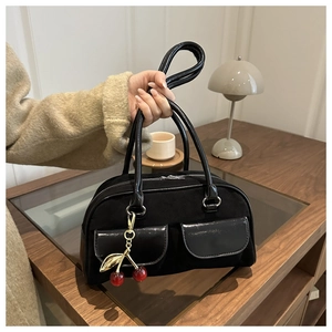 Detail of a black suede handbag featuring pocket designs and a cherry charm