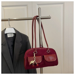Detail of burgundy suede handbag featuring double front pockets and metal cherry charm