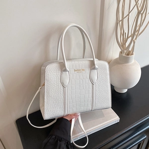 White crocodile pattern tote bag with gold lettering on a minimalist book base