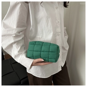 Detail of green quilted makeup bag with diamond pattern held by model in white shirt