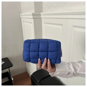 Dettaglio della borsa da trucco trapuntata blu brillante tenuta in mano per mostrare le dimensioni