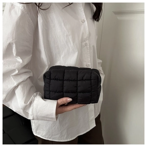 Detailed view of a black quilted makeup bag with square padding held by a person