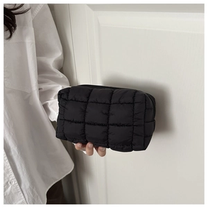 Dettaglio di una trousse nera trapuntata tenuta contro una camicia bianca per scala