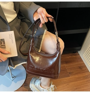 Detail of embossed lettering on brown glossy leather shoulder bag with silver buckle