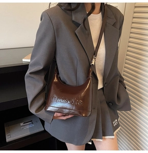 Detail of a brown glossy leather shoulder bag with embossed logo and adjustable strap