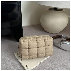 Detail of beige quilted puffer makeup bag with checkerboard pattern on magazine