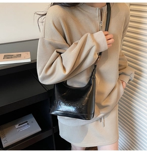 Detail of a black patent leather shoulder bag with embossed lettering on a knit outfit
