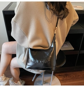 Detail of black glossy leather shoulder bag featuring a stylish embossed letter design