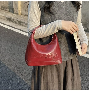 Detail of red glossy leather handbag featuring embossed maische lettering and sleek finish