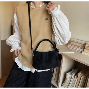 Detail of black pleated suede crossbody bag worn by a model in a cozy library setting