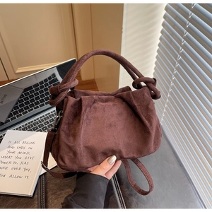Detail of coffee brown pleated handbag with knot handle and adjustable strap in cozy setting