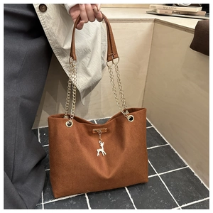 Detail of a brown canvas tote bag with metal chain strap and a white deer pendant