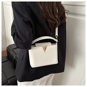 Detail view of white leather bucket bag with gold V buckle worn as a crossbody by model