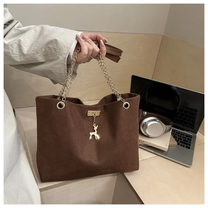 Detail of brown corduroy tote bag featuring gold chain and deer pendant on desktop
