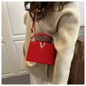 Detail of red leather crossbody bag featuring leopard texture and golden V buckle