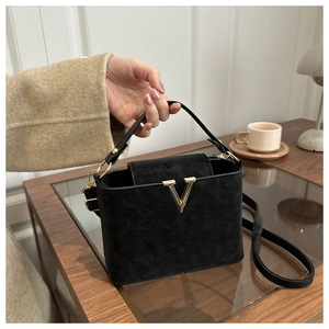 Macro detail of black leather bucket bag featuring a gold V-shaped buckle and strap