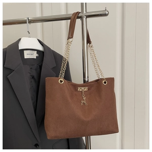 Detail of brown corduroy tote bag featuring gold deer charm and chain shoulder strap