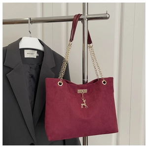 Detail of burgundy corduroy tote bag featuring gold chain strap and deer pendant