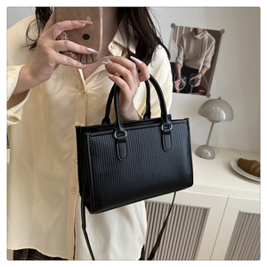 Close-up of black square tote bag featuring vertical stripes texture and silver hardware