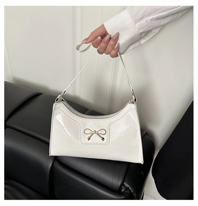 Detail of white patent leather crescent bag featuring a golden bow buckle and smooth texture