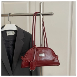 Detail view of burgundy leather boston bag with metallic logo on a grey blazer