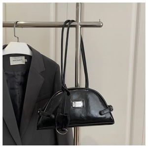 Detail of glossy black crescent underarm bag with metallic plate and dual straps