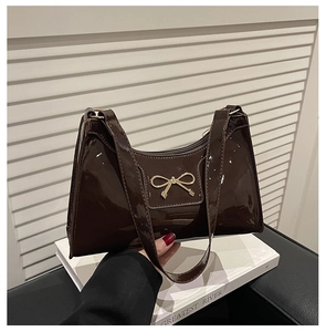 Detail of glossy brown crescent bag featuring gold bow hardware and leather texture